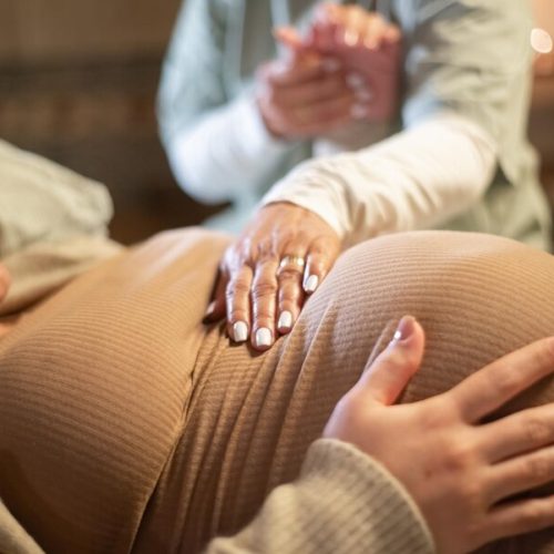 cropped-image-smiling-pregnant-woman-midwife-home-woman-casual-clothes-lying-bed-midwife-holding-hand-pregnancy-medicine-home-birth-concept_74855-24407